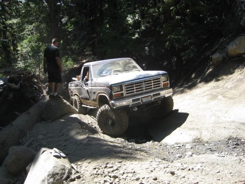 1986 Ford Bronco - This Ford pickup is navigating a challenging off-road trail with large rocks and steep inclines.