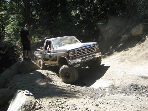 1986 Ford Bronco - A Ford Bronco navigates a rocky, off-road trail with a person standing nearby.