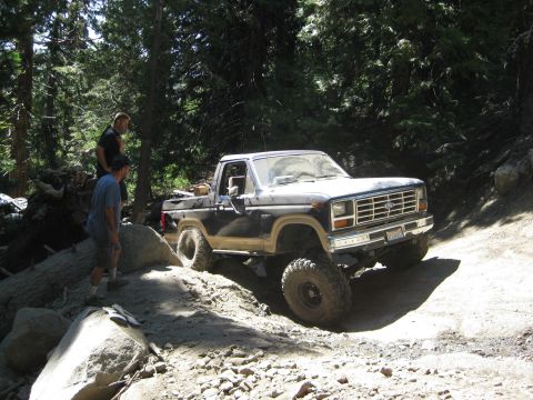 1986 Ford Bronco - 1986 Ford Bronco navigating a challenging off-road path in a forest setting.