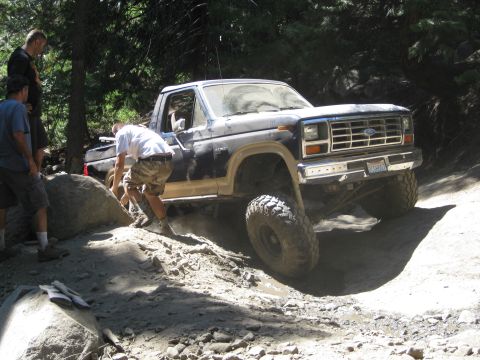 1986 Ford Bronco - A lifted Ford truck navigates a rocky trail with assistance from onlookers.