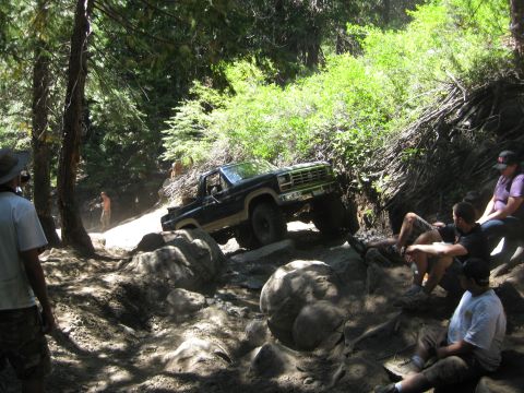 1986 Ford Bronco - A black Ford Bronco tackles a challenging, rocky off-road path with spectators watching.