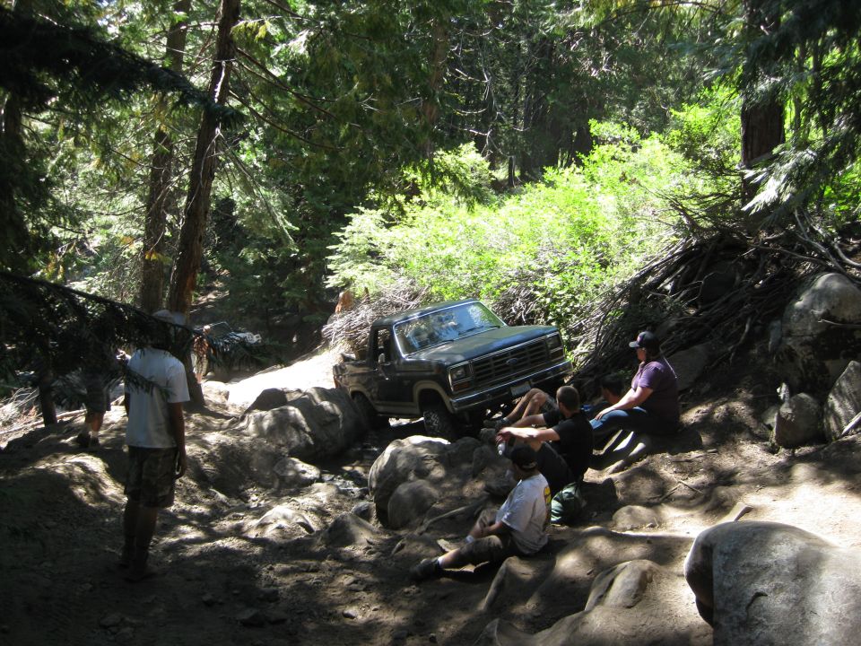 Dark green Ford Bronco navigating a boulder-strewn forest trail with people watching