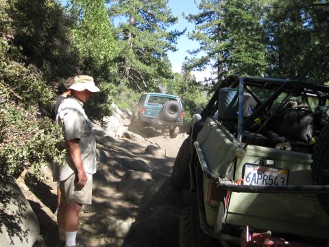 1986 Ford Bronco - A green 1986 Ford Bronco navigates a challenging, rocky off-road trail with another vehicle visible ahead.