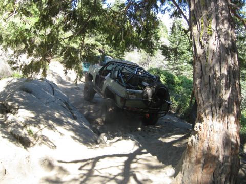 1986 Ford Bronco - A modified off-road vehicle navigates a challenging rocky path under trees.