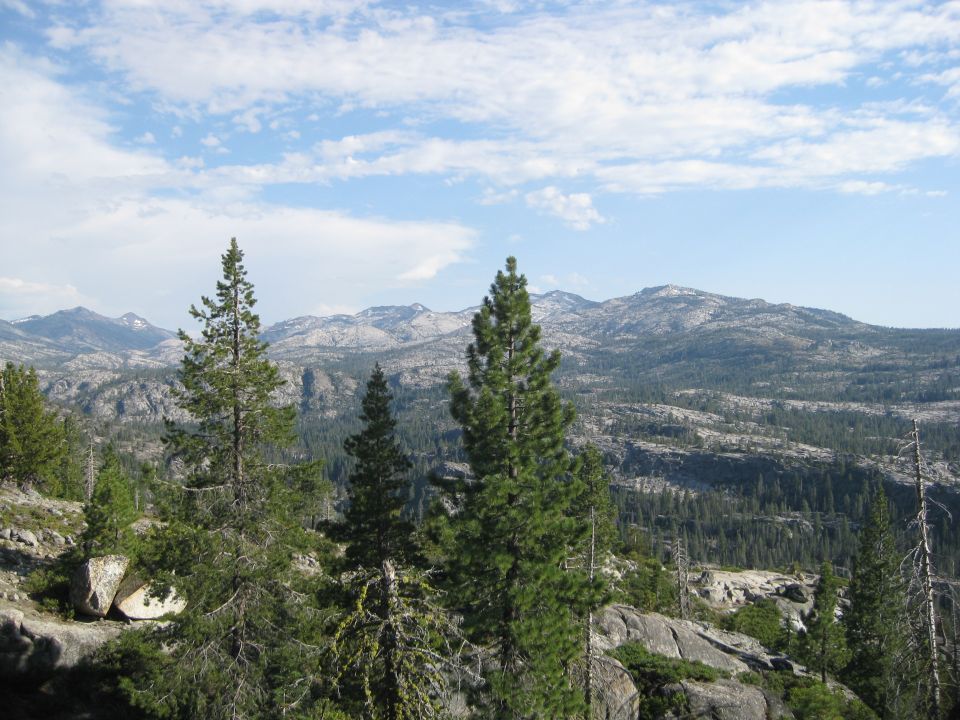 Mountainous terrain with scattered pine trees under a partly cloudy sky