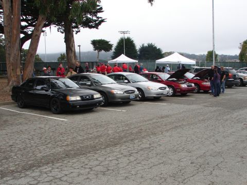 1992 Ford Taurus - Multiple Ford Taurus sedans are parked in a lot, some with hoods open, under an overcast sky.