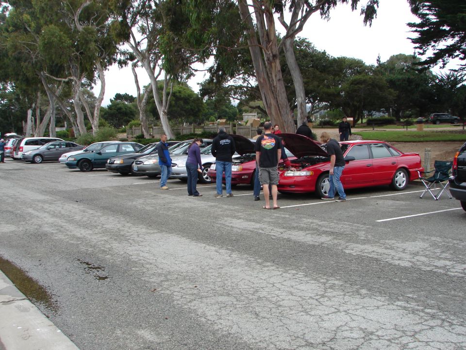 red sedan with hood up, people looking at engine, parked next to other cars