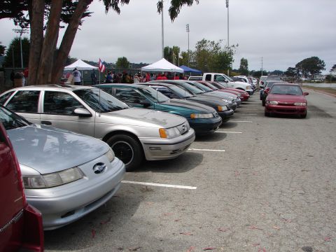 1992 Ford Taurus - A line of cars, including a silver 1992 Ford Taurus, are parked at an outdoor event.