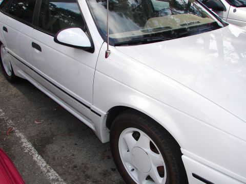 1992 Ford Taurus - A white 1992 Ford Taurus sedan is parked outdoors, showing its front three-quarter view with a black pinstripe and body kit.