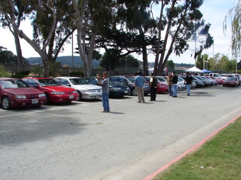 1992 Ford Taurus - A line of cars, including a red 1992 Ford Taurus, are parked outdoors at an event.