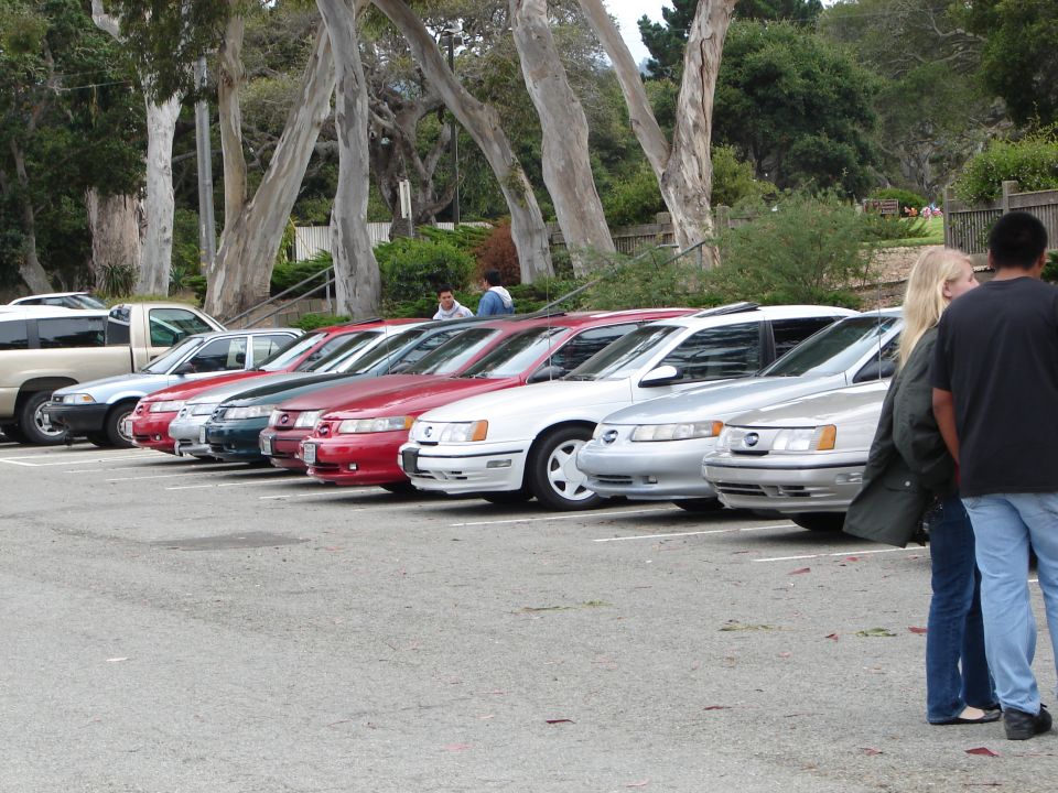 Several sedans parked in a lot, some people standing nearby