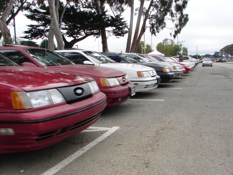 1992 Ford Taurus - A line of Ford Taurus sedans are parked in a lot, with the front of the closest red car prominently displayed.