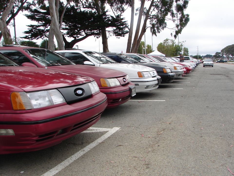 Several Ford Taurus cars parked in a row, front view of the closest red one