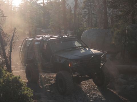 1991 Ford Bronco - Modified SUV navigates a dusty, rocky trail in a wooded area.