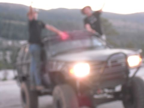 1991 Ford Bronco - Two people are on top of an off-road vehicle with its headlights illuminated.