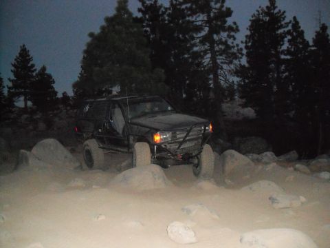 1991 Ford Bronco - Modified SUV with a prominent roll cage traverses a challenging rocky path during twilight hours.