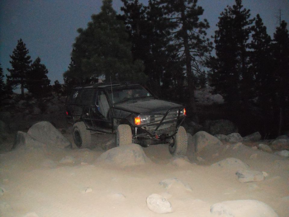 Black SUV with roll cage navigating rocky terrain at dusk