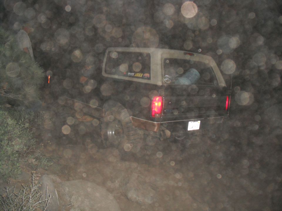 Rear view of a 1991 Ford Bronco on a dirt trail at night. It has a sticker on the rear window that says 'PURE JEGS'