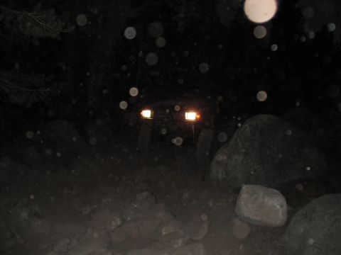 1991 Ford Bronco - An off-road vehicle navigates a rocky trail in the dark, illuminated by its headlights.