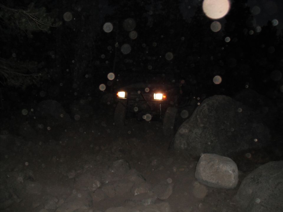Dark off-road vehicle with headlights on, driving on a rocky path at night