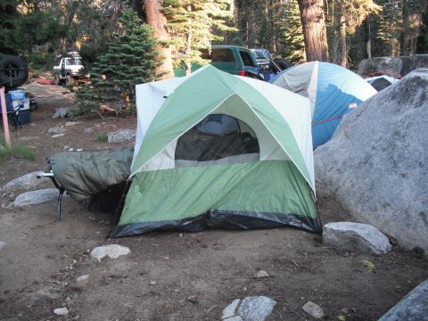 1991 Ford Bronco - Two SUVs are parked at a campsite, surrounded by trees and tents, suggesting an outdoor adventure.