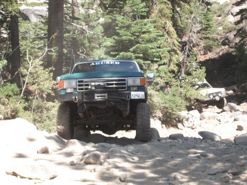 1991 Ford Bronco - This modified truck navigates a challenging, rocky trail surrounded by trees.