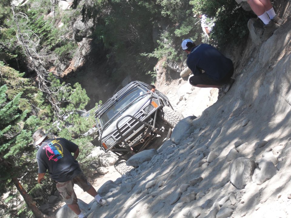 Gray off-road SUV with a roll cage climbing a rocky incline, front view