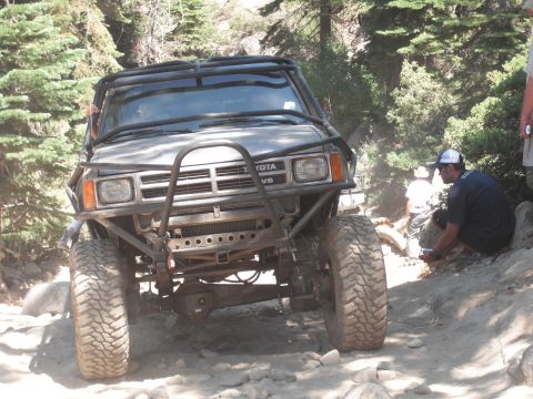 1991 Ford Bronco - A modified Toyota truck navigates a challenging off-road trail with onlookers present.