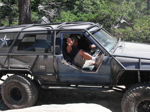 1991 Ford Bronco - A heavily modified off-road vehicle navigates a rocky trail with its driver visible through the open door.
