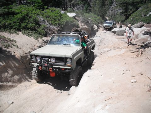 1991 Ford Bronco - An olive green off-road truck maneuvers through a challenging rocky terrain with another vehicle following behind.