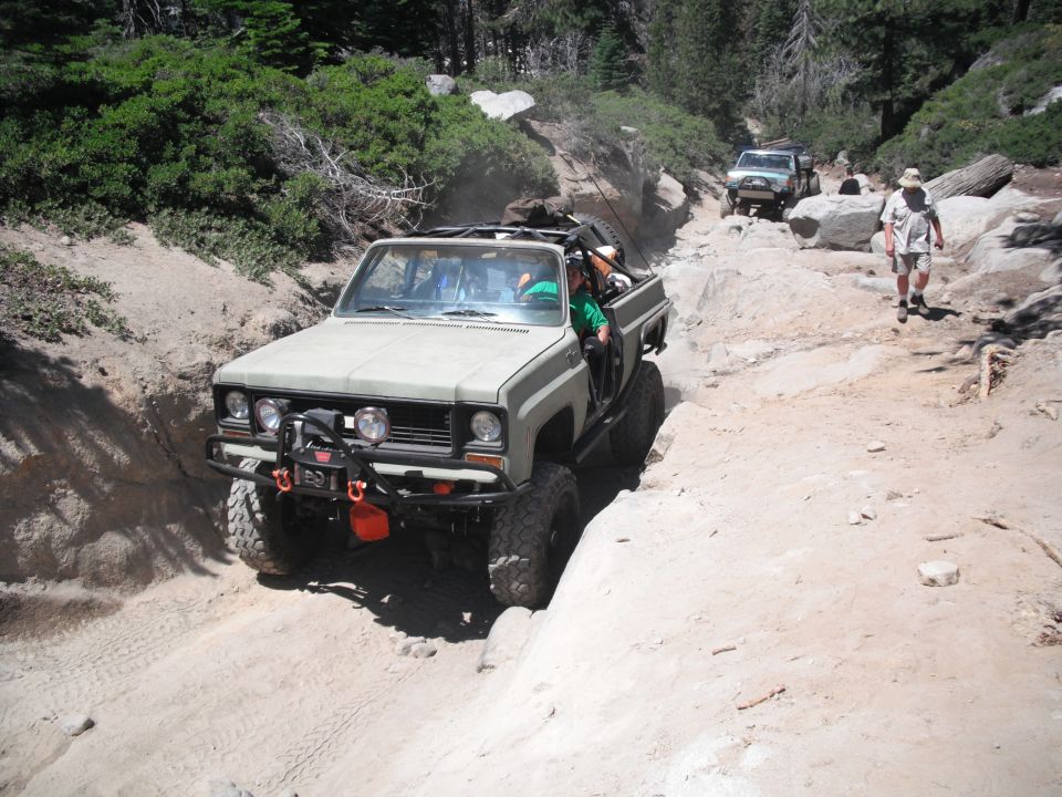 Olive green off-road truck with a winch and orange tow hooks navigating a rocky trail