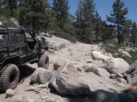 1991 Ford Bronco - Off-road vehicle navigates a challenging rocky trail under a clear blue sky.