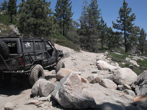 1991 Ford Bronco - This heavily modified SUV navigates a challenging rocky path in a mountainous, wooded area.