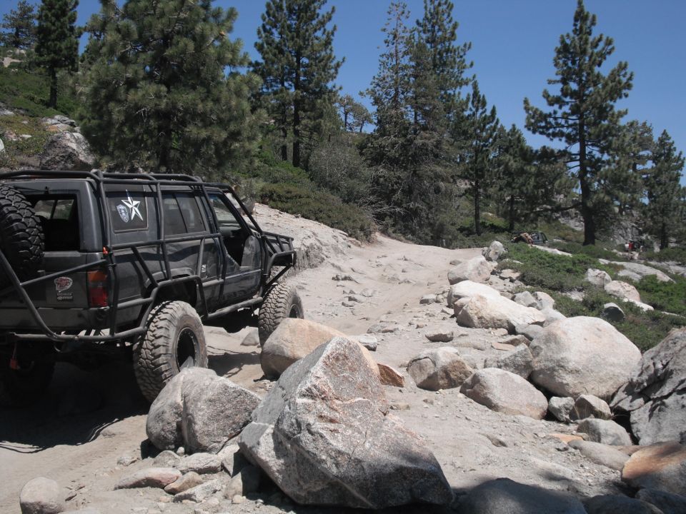 Modified off-road SUV with external roll cage and spare tire on a rocky trail