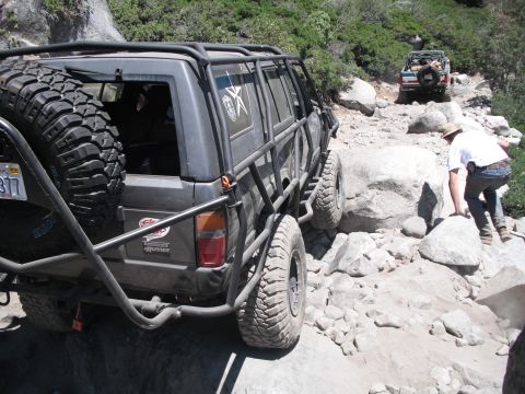 1991 Ford Bronco - Two off-road vehicles navigate a challenging rocky trail with a person climbing over boulders.