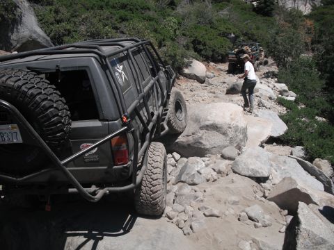 1991 Ford Bronco - An off-road SUV with extensive modifications navigates a challenging rocky trail, with another vehicle visible further up the path.