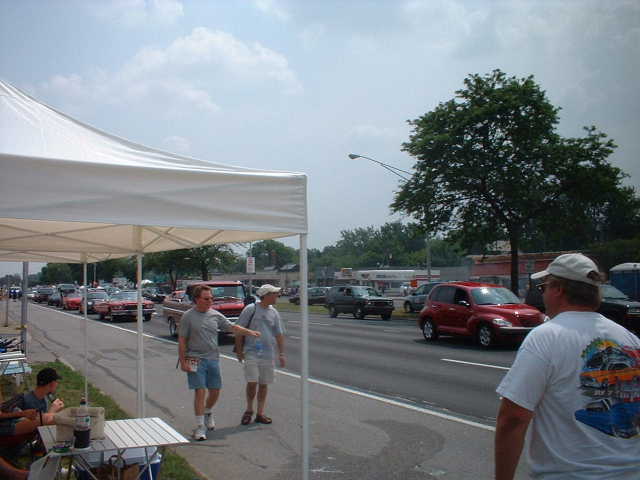 People watching cars lined up on a street under a tent