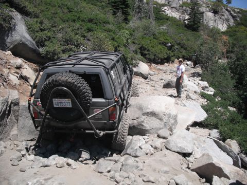 1991 Ford Bronco - An off-road SUV navigates a challenging rocky trail, with a person observing the vehicle's progress.