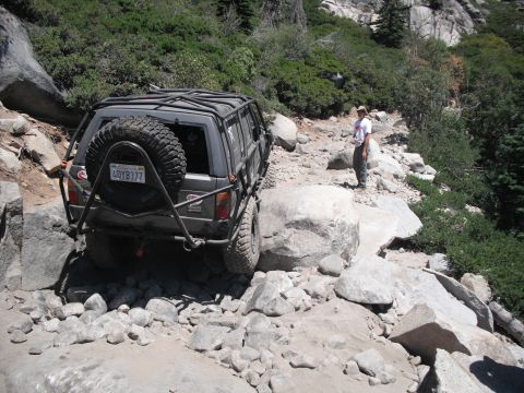 1991 Ford Bronco - A person stands on a rocky mountain path next to a modified off-road vehicle.