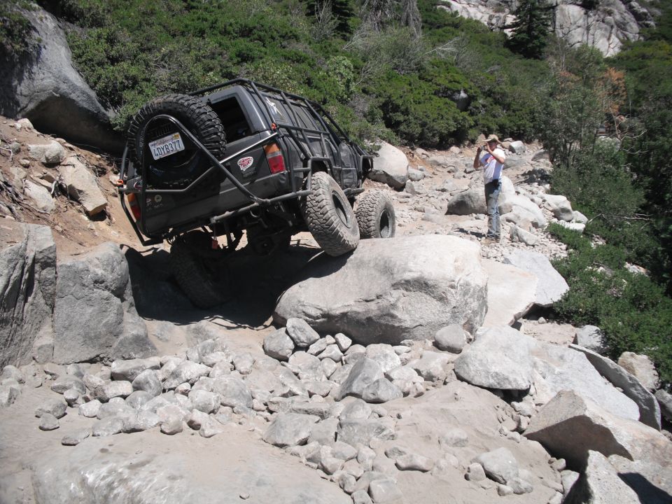 Black off-road vehicle with external roll cage and spare tire on rocky trail