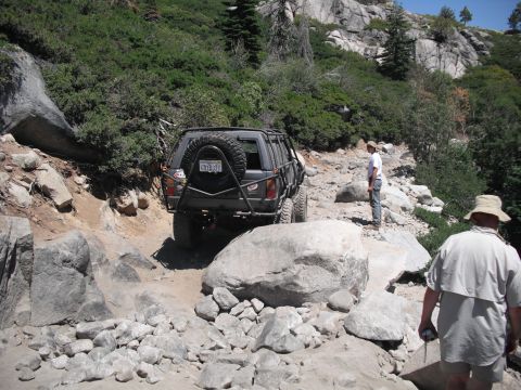 1991 Ford Bronco - An off-road vehicle tackles a difficult rocky path in a mountainous, wooded area.
