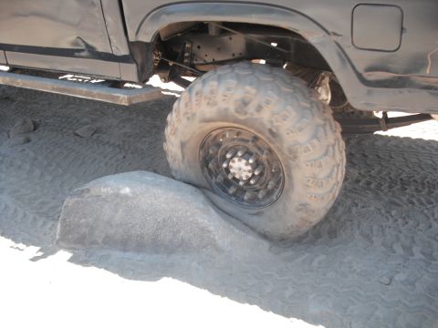 1991 Ford Bronco - A vehicle's large tire is stuck on a rock while driving on sandy terrain.