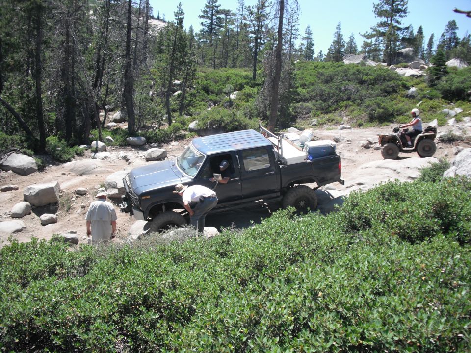 Dark blue pickup truck with a camper shell on a rocky trail, front passenger side tire is off the ground
