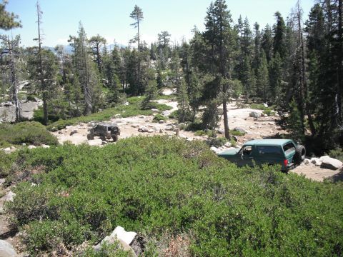 1991 Ford Bronco - Two SUVs navigate a rocky, wooded trail during the day.