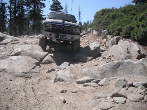 1991 Ford Bronco - A dark SUV navigates a challenging rocky terrain on a sunny day.