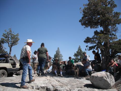 1991 Ford Bronco - A group of people and an off-road vehicle are gathered on a rocky, wooded terrain under a clear blue sky.