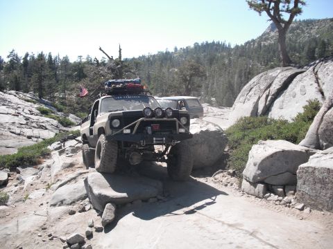 1991 Ford Bronco - A modified off-road truck navigates a challenging rocky terrain with another vehicle visible in the background.