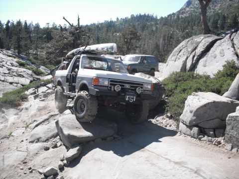 1991 Ford Bronco - This modified Ford truck is tackling a challenging rocky trail with a kayak secured to its roof rack.