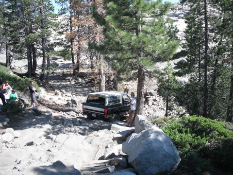 1991 Ford Bronco - A Ford Bronco navigates a challenging rocky terrain with trees and people nearby.