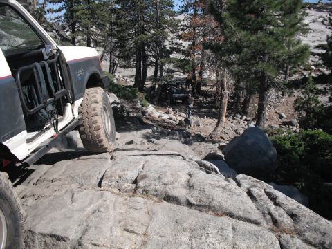 1991 Ford Bronco - Two off-road vehicles tackle a challenging rocky path in a wooded area.